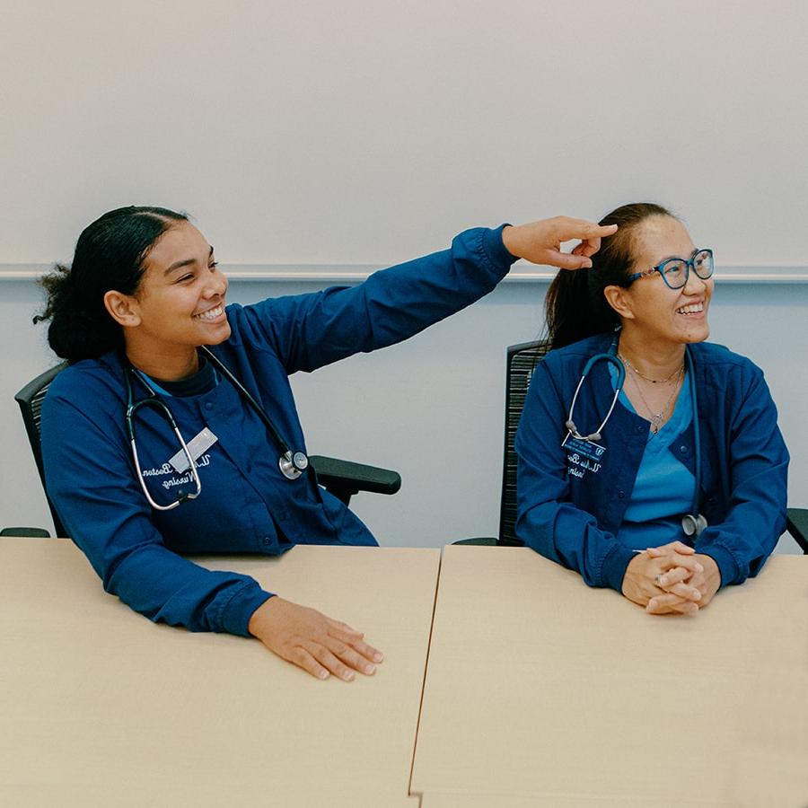 nursing student pointing toward front of class while other student looks on